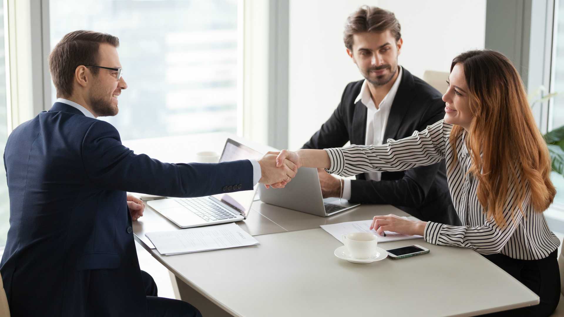  A lawyer and his client shake hands after successfully negotiating a personal injury settlement while a paralegal looks on.